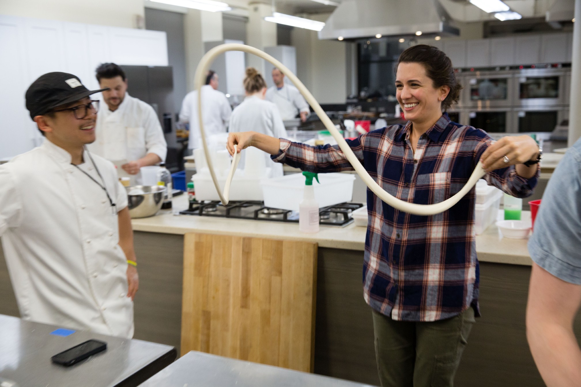 Cook's Science associate editor Tim Chin, left, looks on as managing editor Kristin Sargianis swings a rope of dough through the air to stretch it out as they practice a technique for making hand-pulled noodles.