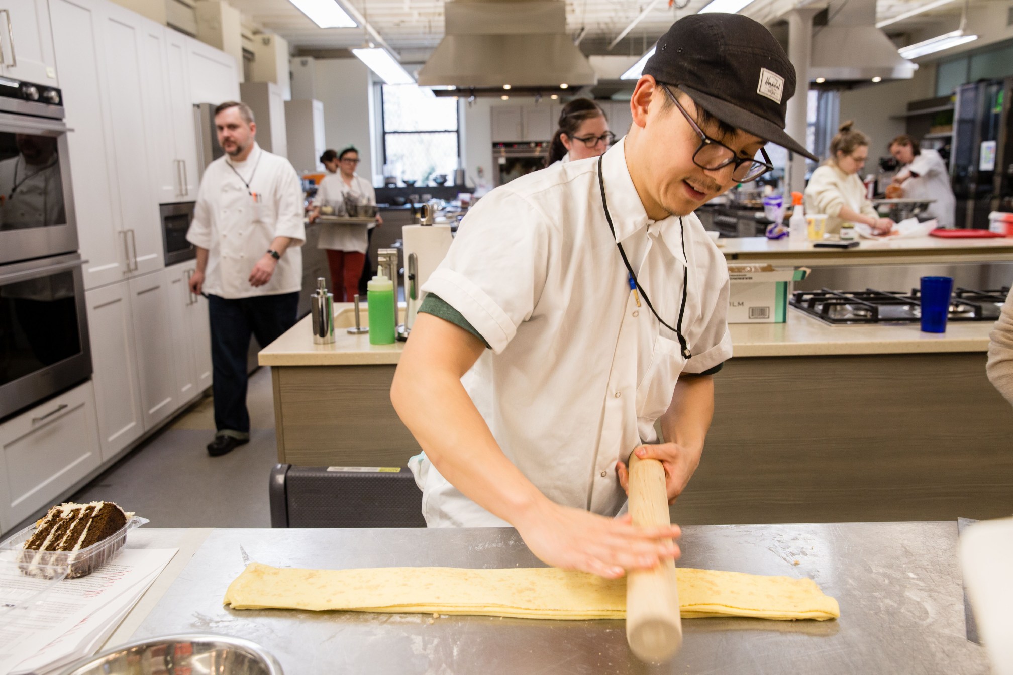 Cook's Science associate editor Tim Chin uses a rolling pin to compress four stacked sheets of pastry dough brushed with butter and sprinkled with sugar while working on an in-development recipe for laminate pastry.