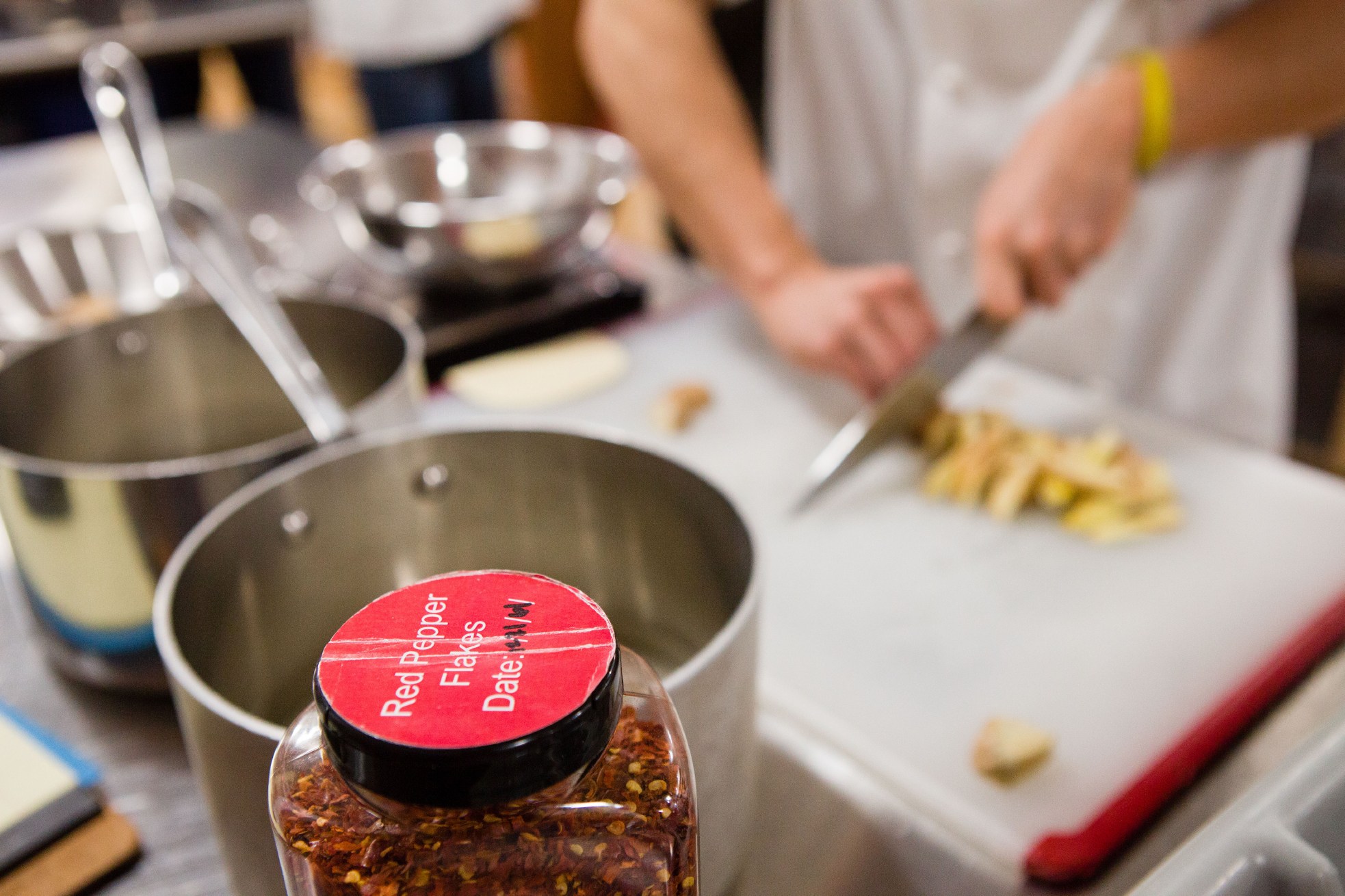 Pepper flakes sit in the foreground ready to use as associate editor Tim Chin slices ginger. The spiciness of ginger dissipates over time so Tim is experimenting with ways to infuse heat back into a dish that relies on the root of this flowering plant.